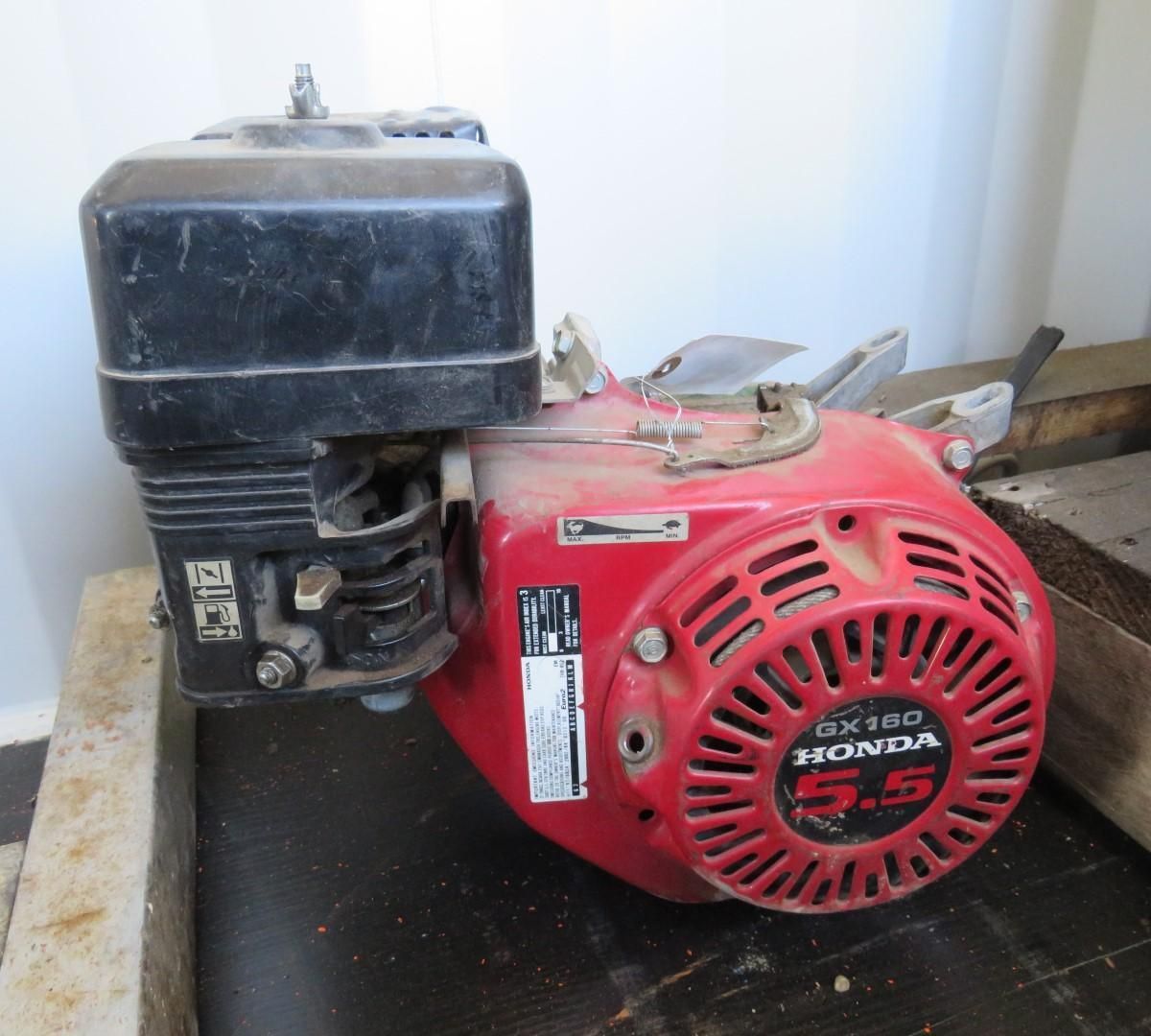 Red Honda GX100 5.5 engine. Black air filter atop. Dusty, on wooden surface.