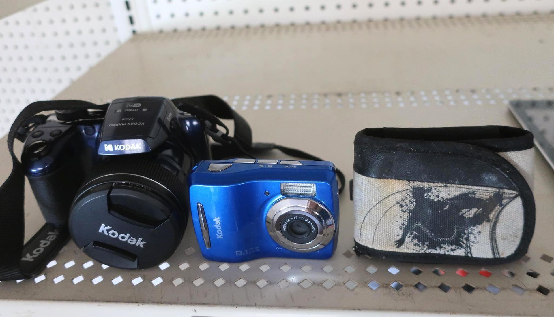 Three cameras on a shelf: a black Kodak, a blue camera, and a case.