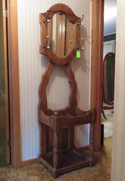 Wooden hall tree with oval mirror, coat hooks, and umbrella stand.