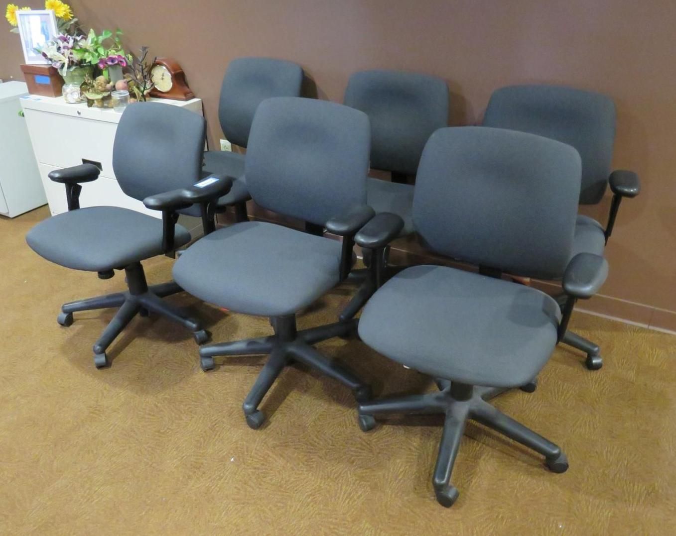 Six dark gray office chairs on a brown floor, arranged in a group.