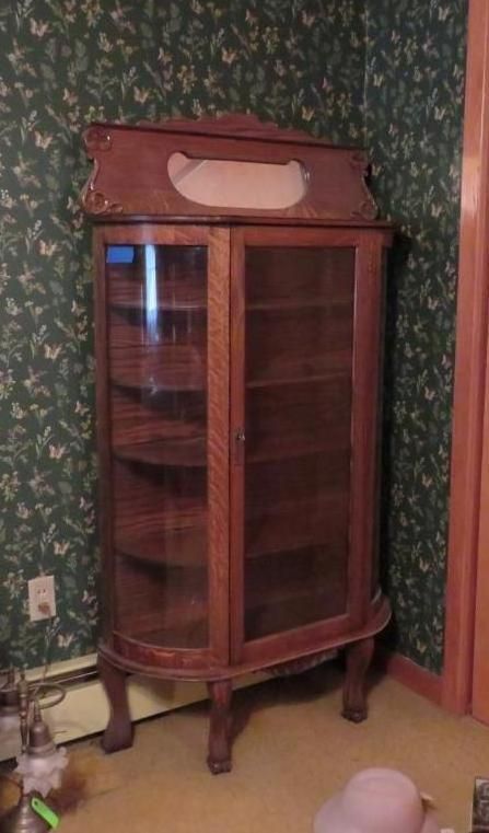 Antique wooden display cabinet with glass doors and shelves, set in a room with patterned wallpaper.