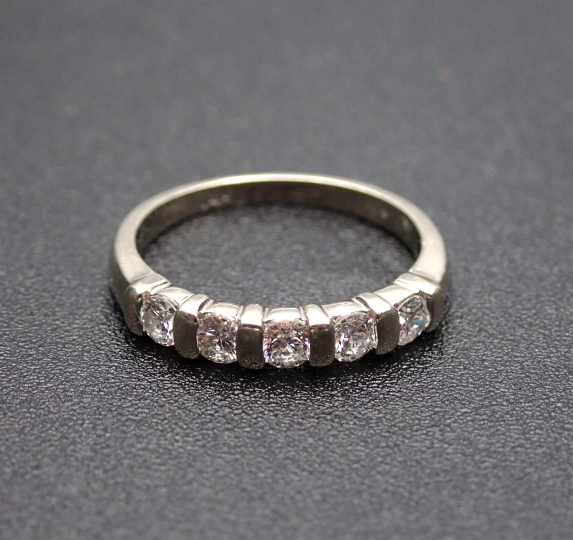Silver ring with five clear gemstones set on a dark surface.