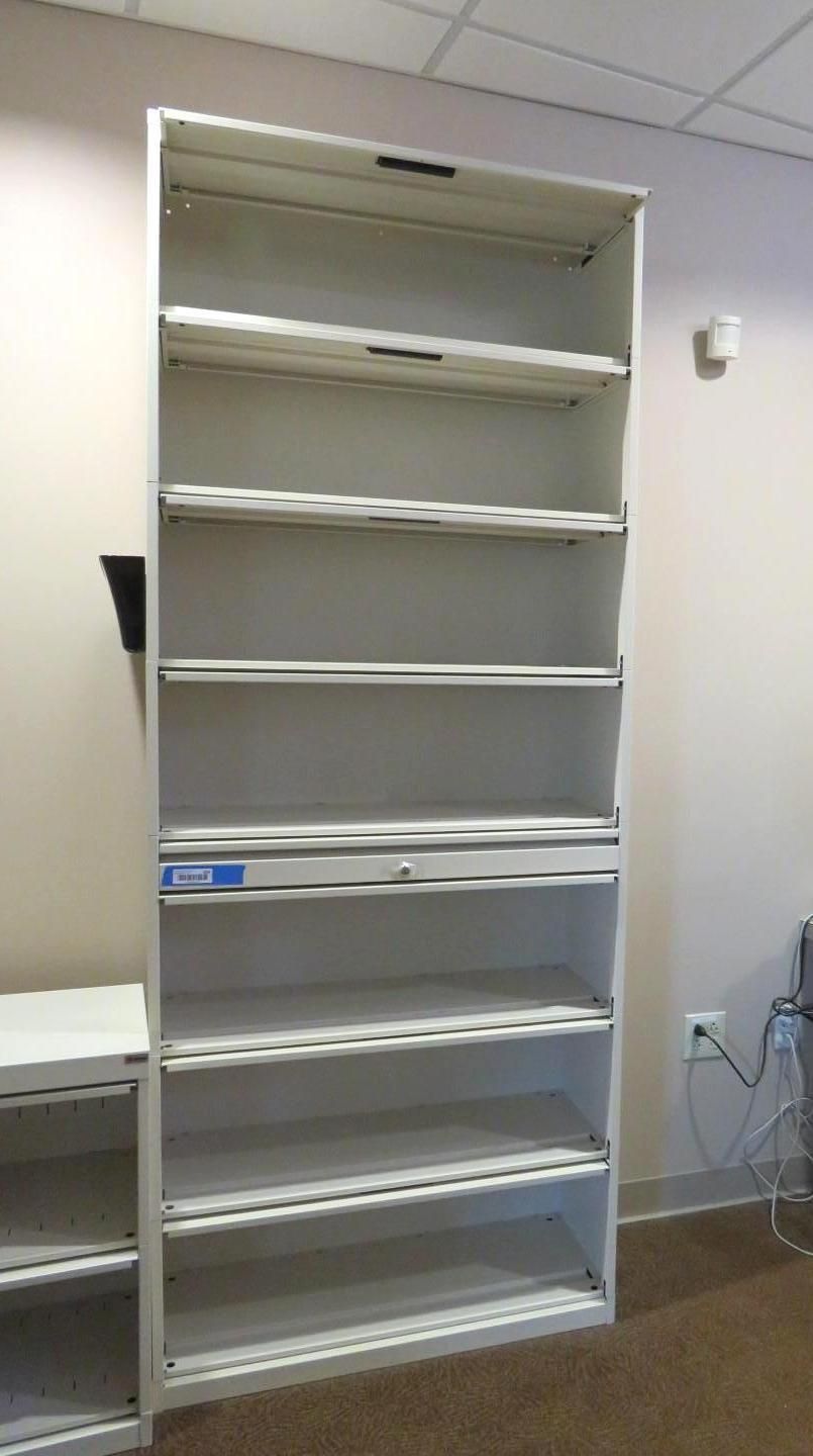 Tall, empty, light-colored metal shelving unit against a wall in a room.