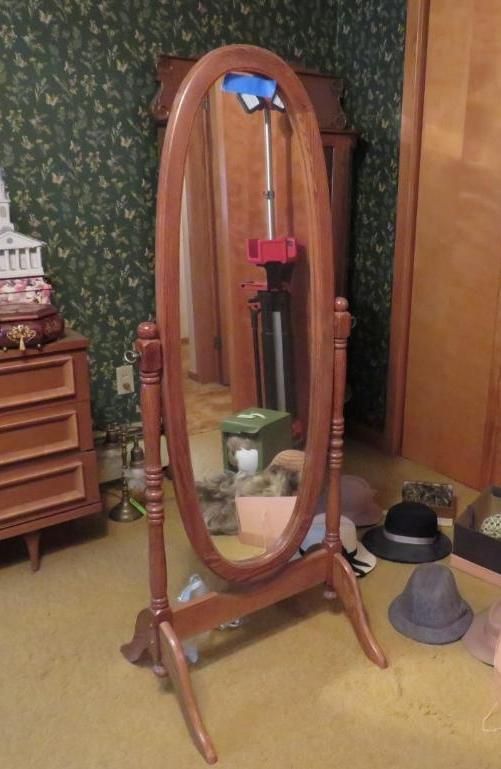 Wooden oval-shaped standing mirror in a room.