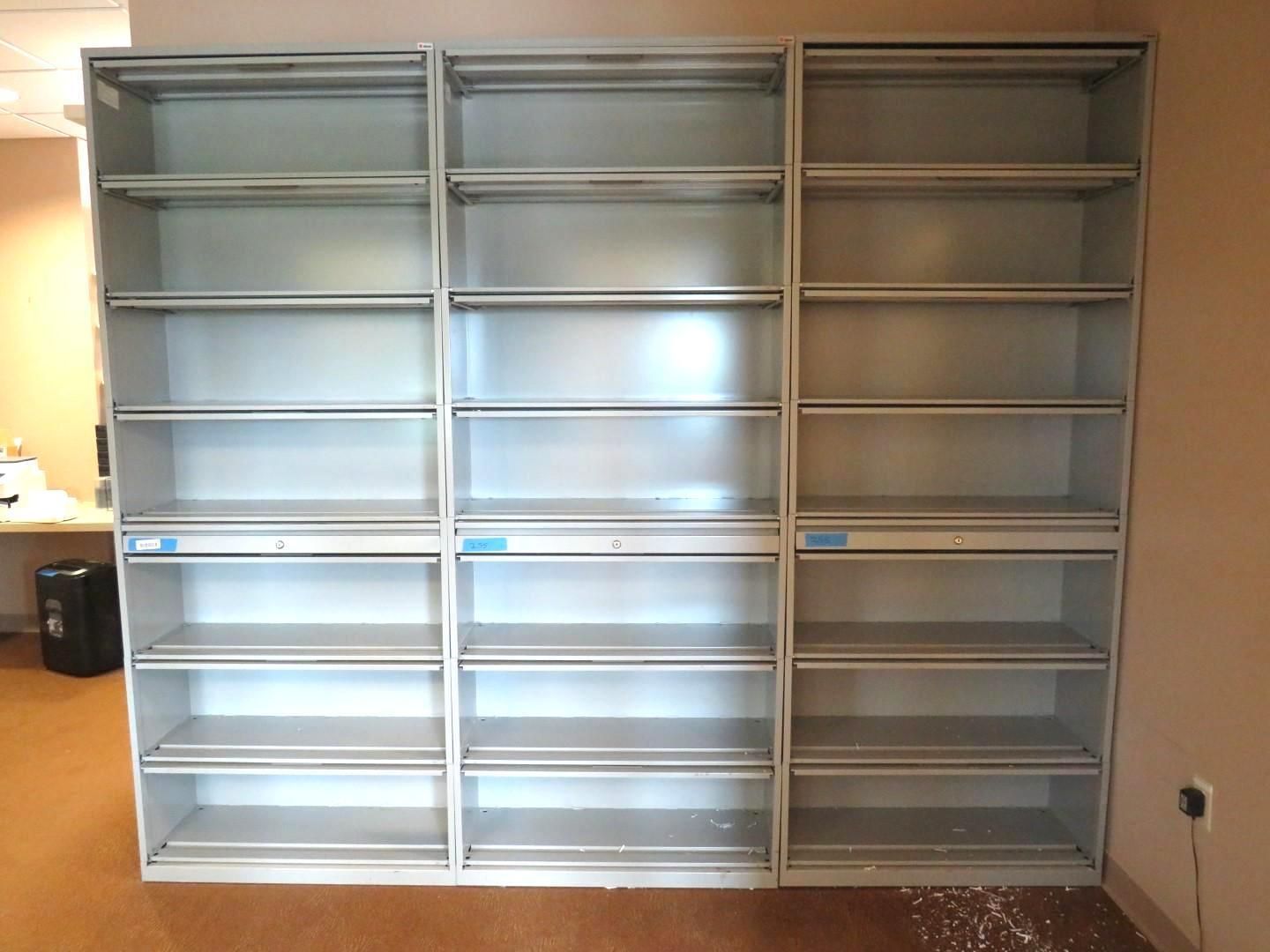 Three empty gray metal shelves attached to a beige wall.