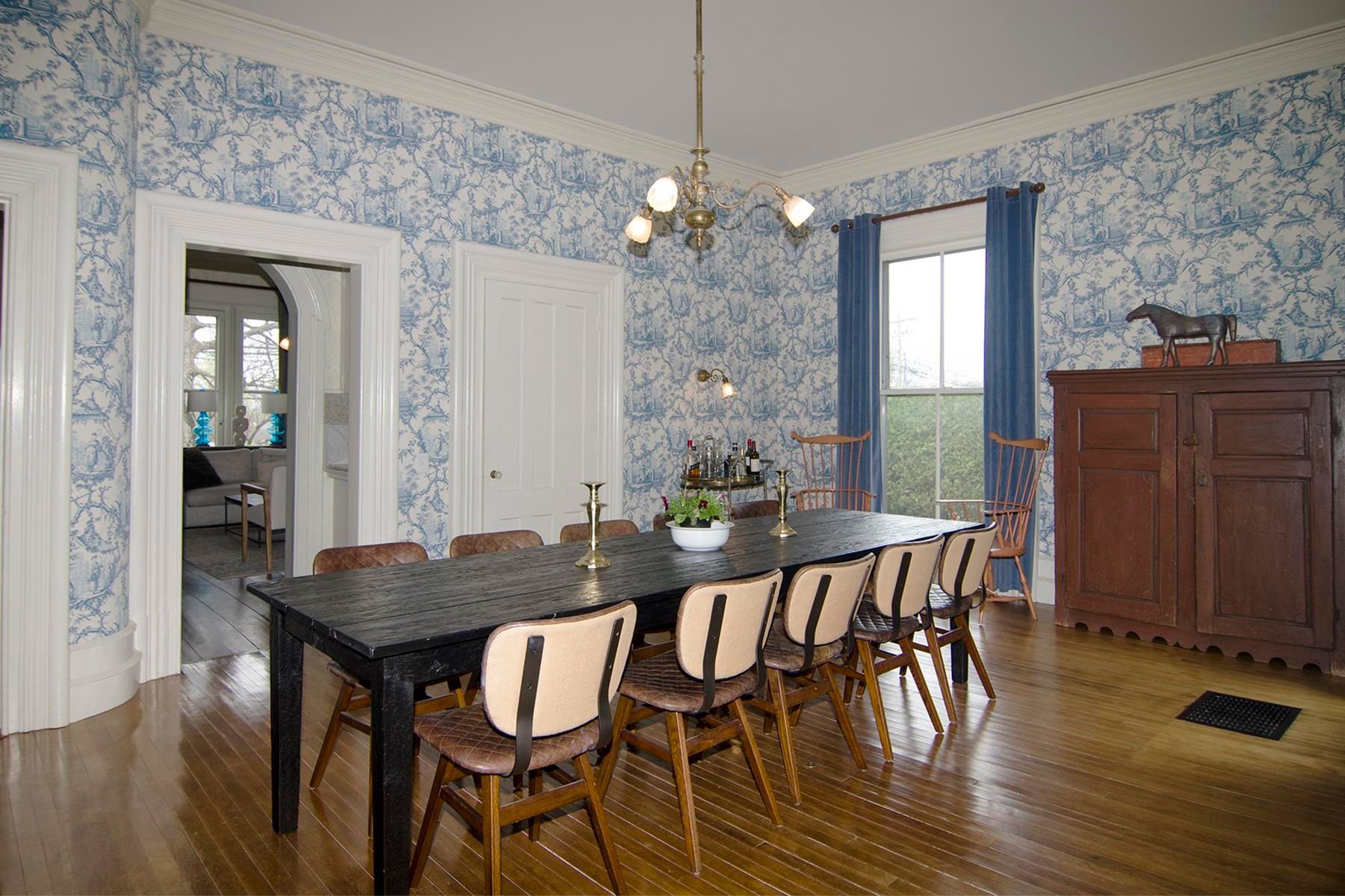 Dining room with blue floral wallpaper, a dark table, chairs, and a wooden cabinet.