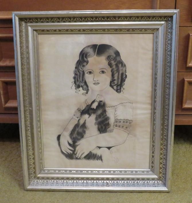 Framed pencil portrait of a girl with curly hair holding a cat. Silver frame on a light background.