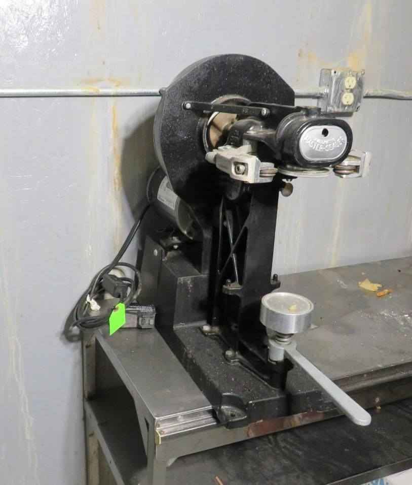 Black industrial machine with a grinding wheel and magnifying lens, mounted on a metal base, on a workbench.