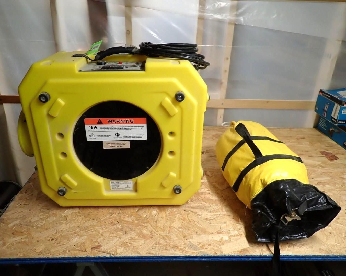 Yellow ventilation fan and attached black air sock on a wooden surface.