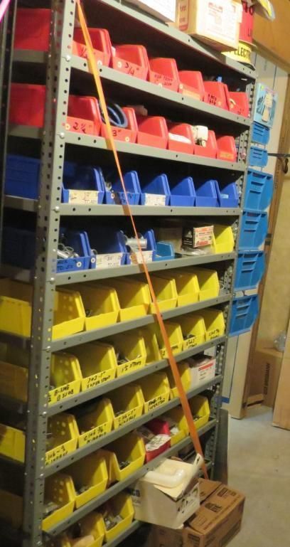 Metal shelving unit with red, blue, and yellow bins. Orange strap secures the top, items stored.