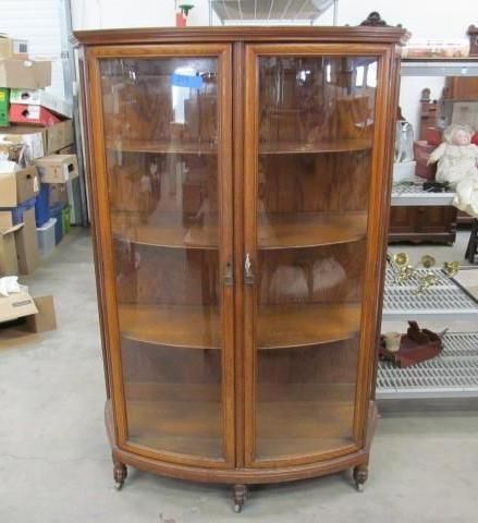 Wooden curio cabinet with curved glass doors and shelves.