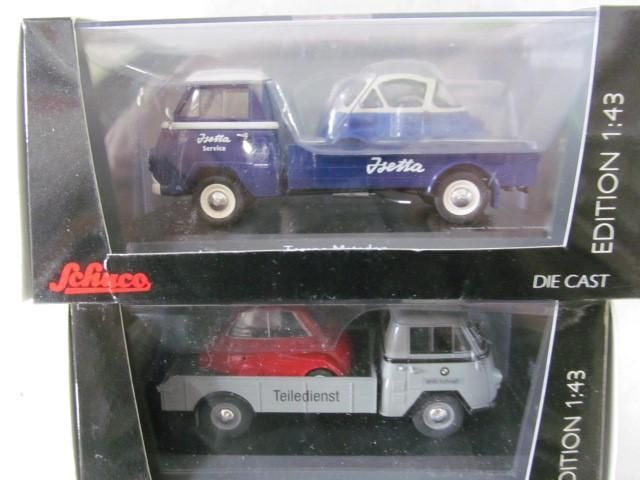 Two die-cast model car sets in boxes. One blue transporter with a small white car, the other grey with a red car.