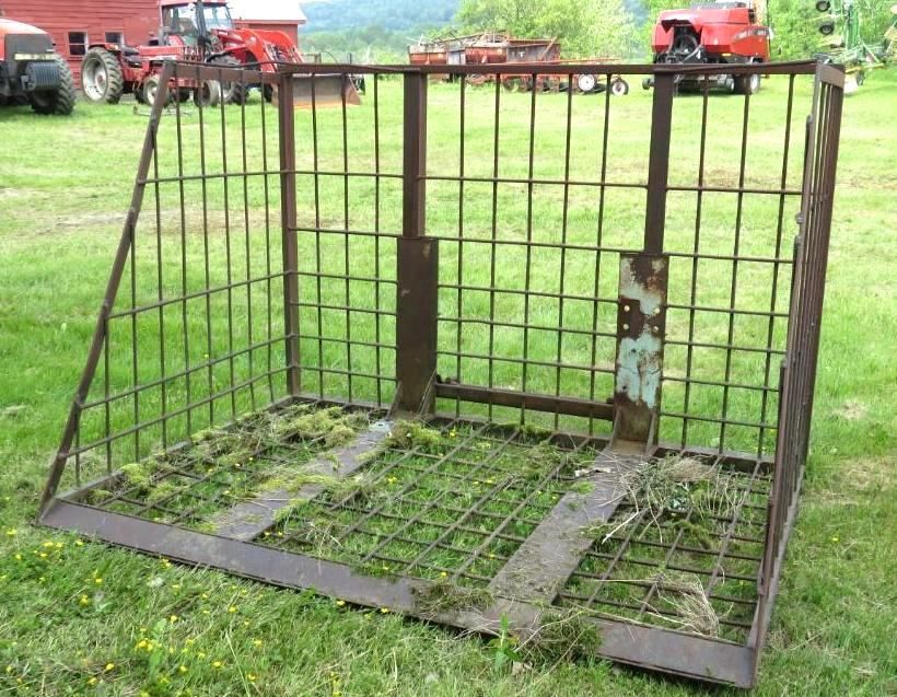 Metal cage with a wire mesh floor, likely for transporting objects on a farm, outdoors on grass.