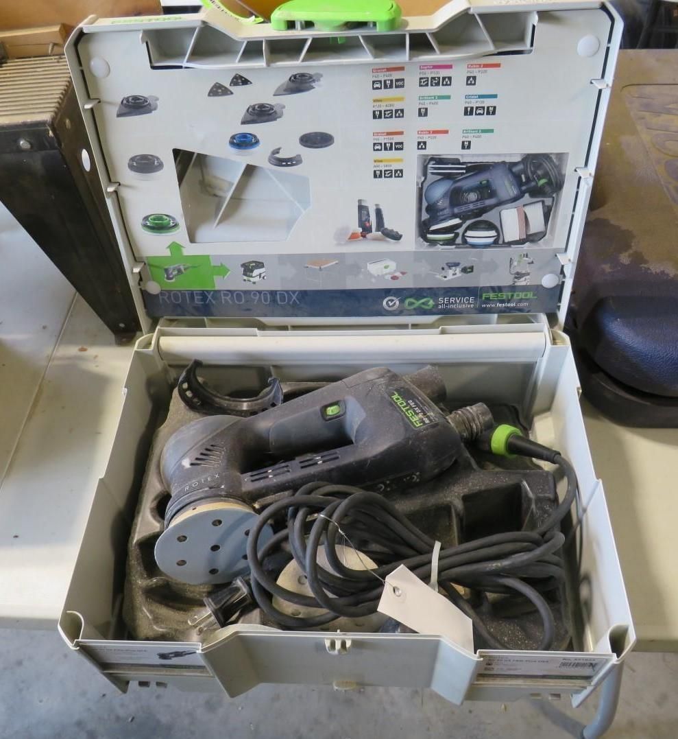 Open white case containing a black and green power sander with its cord.