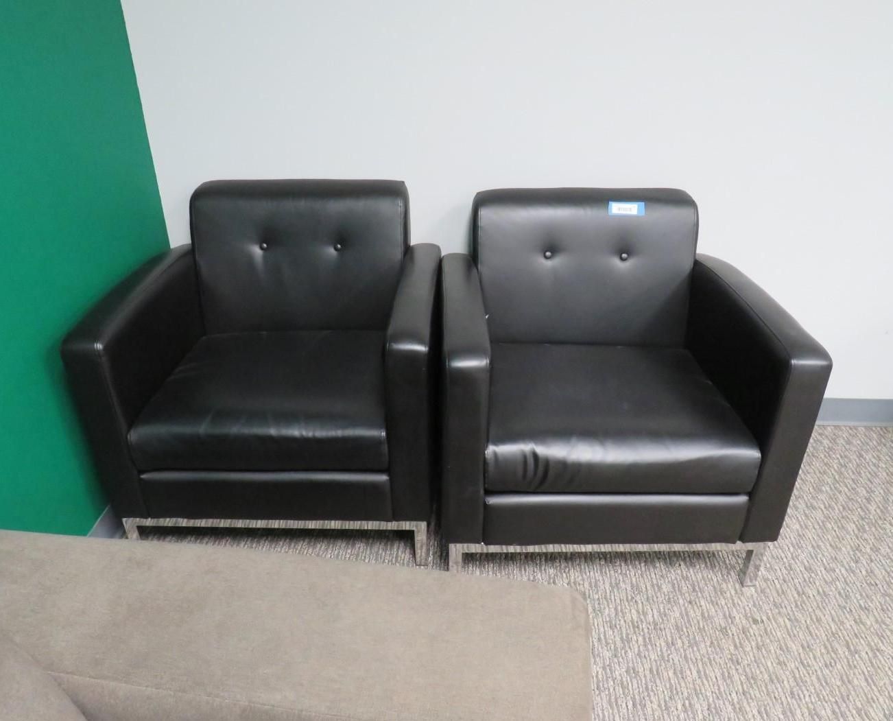 Two black leather armchairs with silver legs sit side-by-side on a beige carpet.