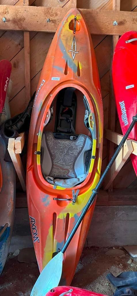 Orange kayak with a paddle inside a wooden shed.