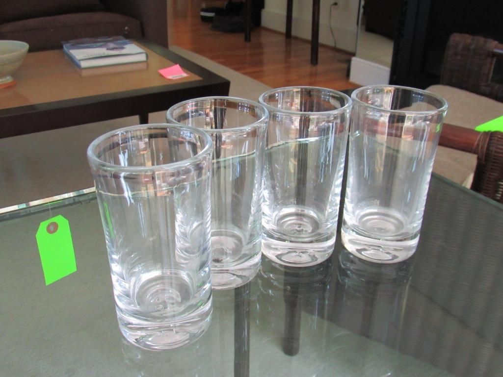 Four clear glass tumblers with silver rims on a glass table.