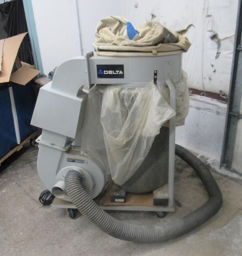 A Delta dust collector, gray, with a hose and bag attached, in a workshop setting.