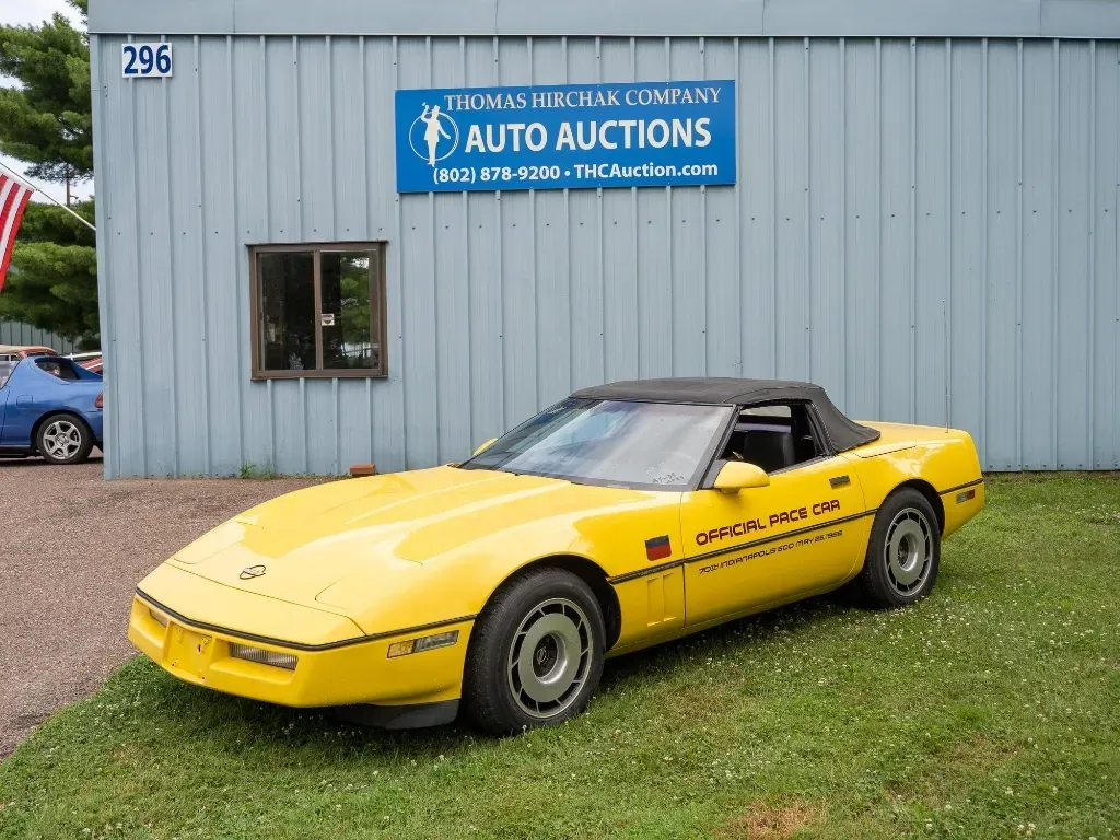 Yellow convertible Corvette parked in front of an auto auction building.