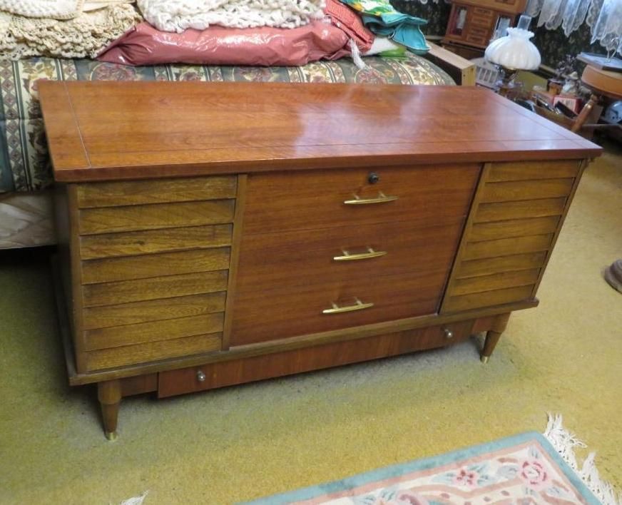 Wooden mid-century modern chest with three drawers and slatted side panels, sitting on a yellow rug.