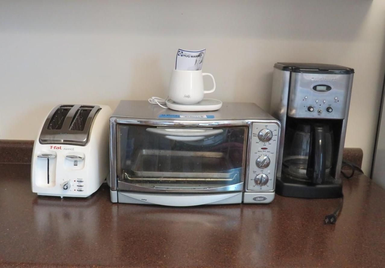 Toaster, toaster oven, and coffee maker on a countertop, with a mug on top of the toaster oven.