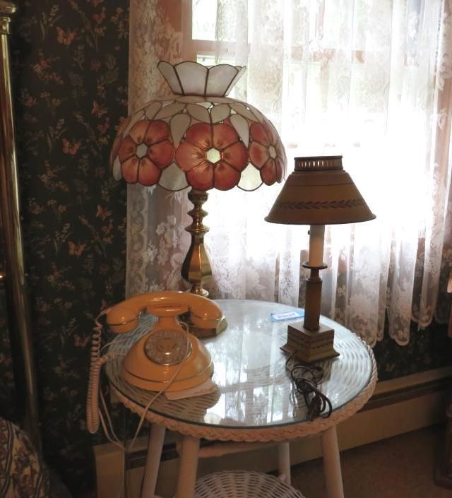 Yellow rotary phone, floral lamp, and small wooden lamp on a round table near a window.