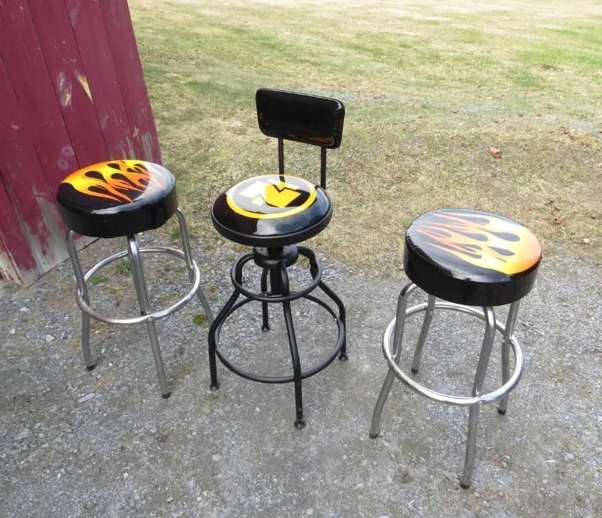 Three flame-decorated bar stools: two chrome-legged, one black with a back. Outdoor setting.