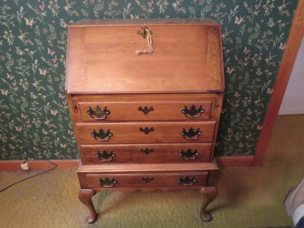 Wooden secretary desk with drawers and a slanted top, on a green carpet in front of a patterned wall.