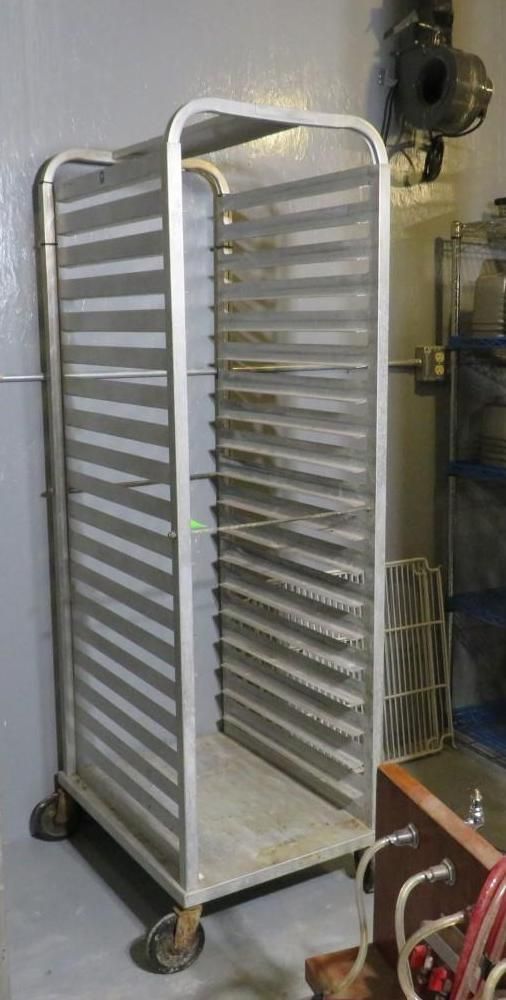 Metal tray rack on wheels in a room, with multiple horizontal slots.