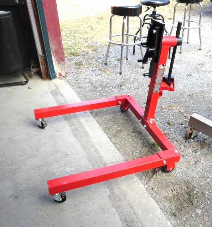 Red engine stand on a concrete surface, with black stools in the background.