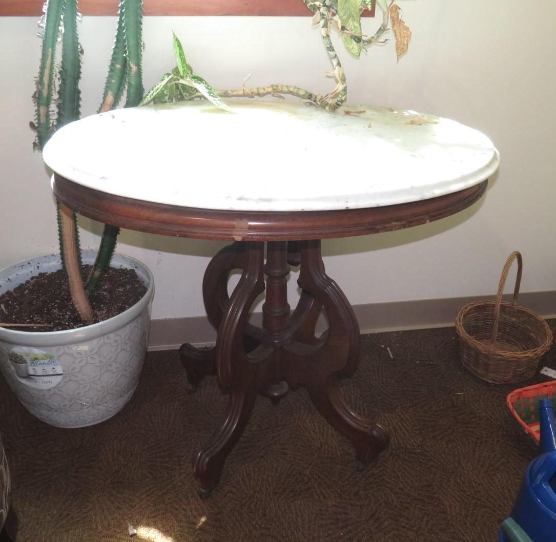 Round antique table with a white top and dark wooden base, next to a potted plant.