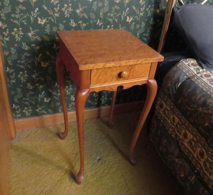 Wooden side table with a drawer and curved legs.