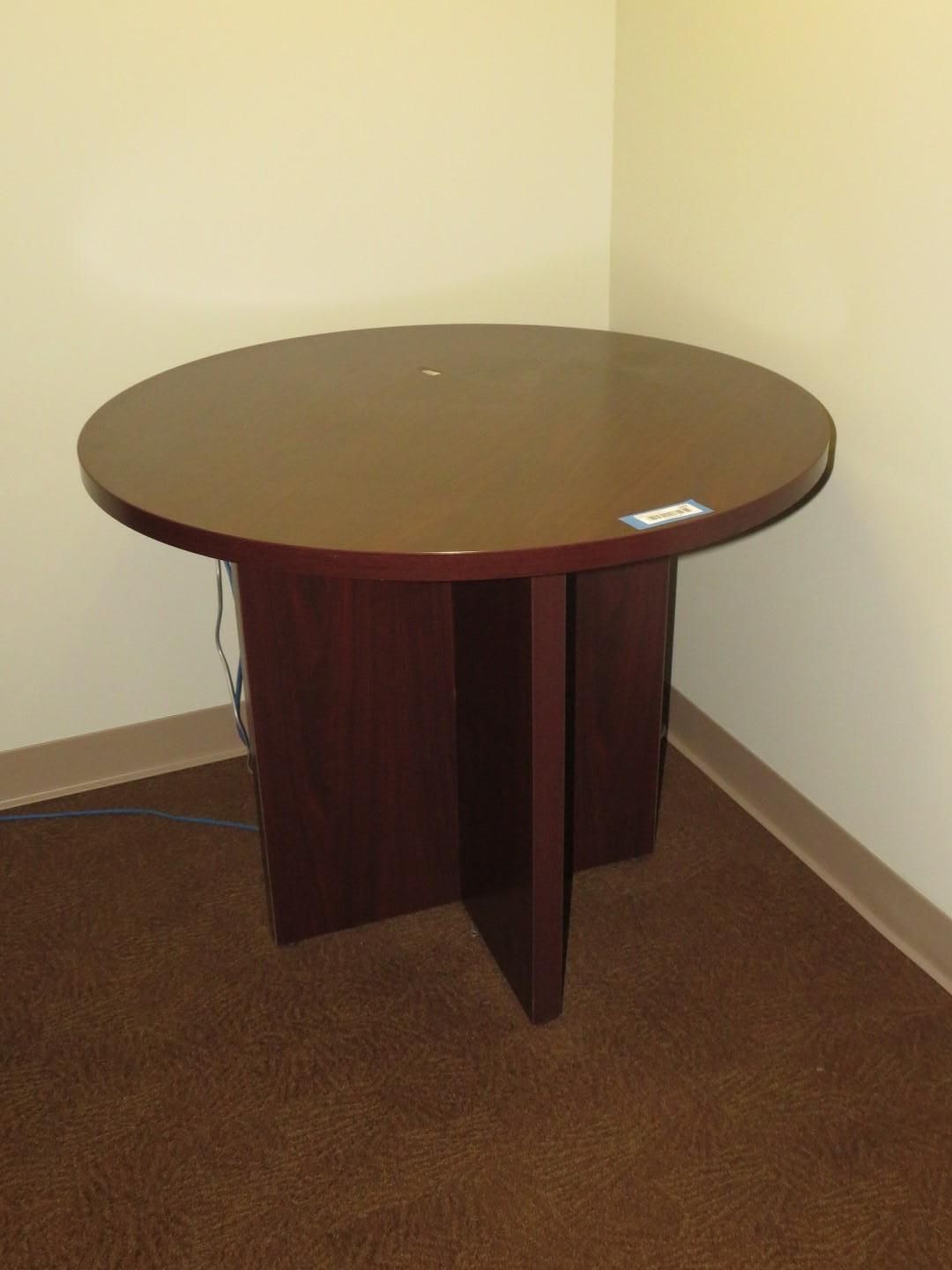 Round, dark wood table in corner of room, sitting on brown carpet with beige walls.