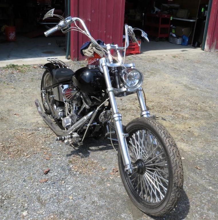 Black and chrome chopper motorcycle parked in front of a red barn.