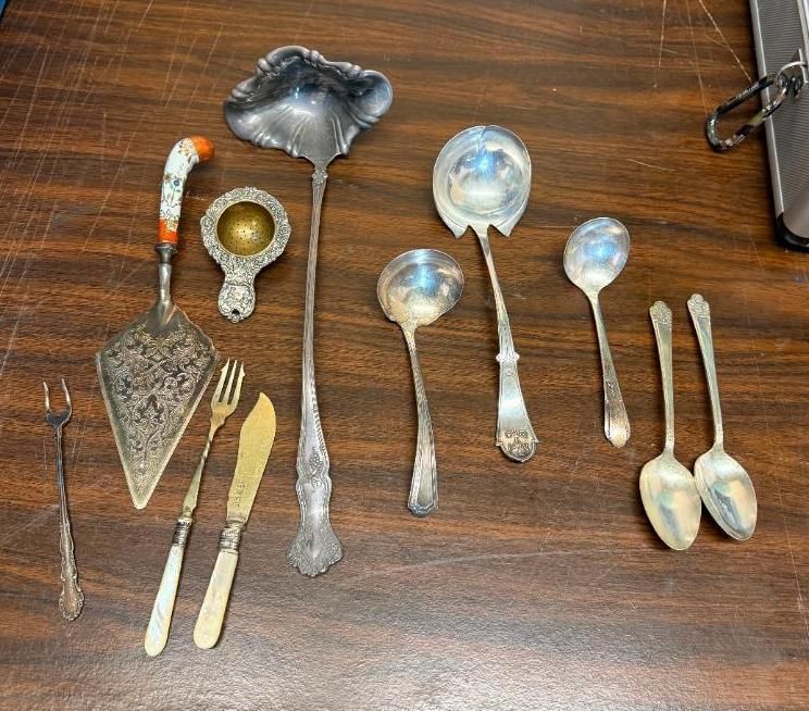 Assorted silver serving utensils and flatware arranged on a wooden table.