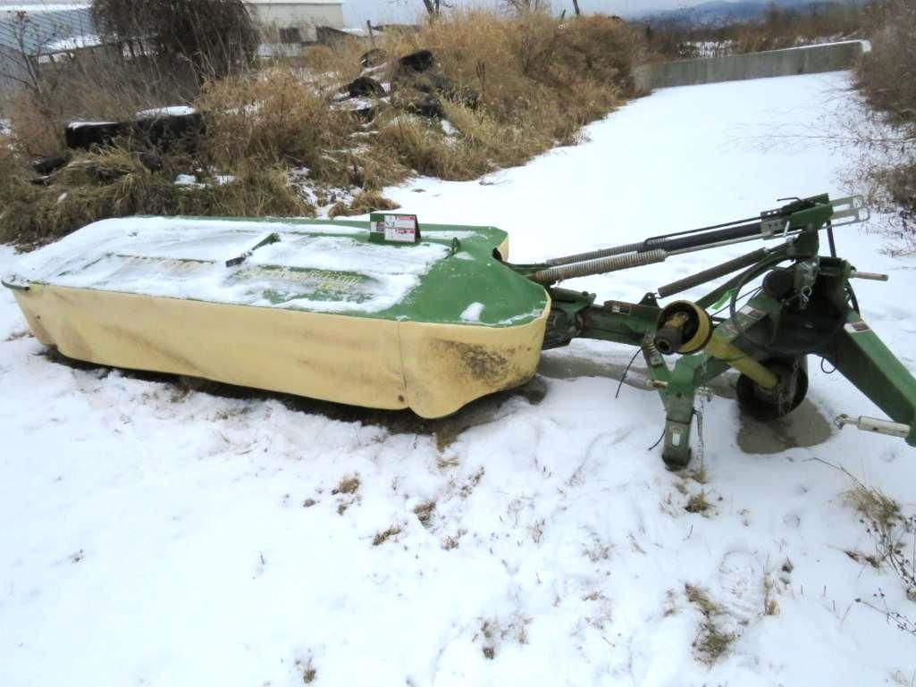 Green farm mower in a snowy outdoor setting.
