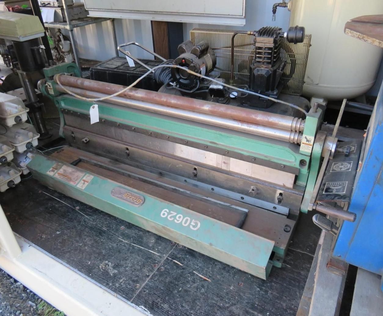 Green metal sheet metal machine with rollers and gauges; outdoors.