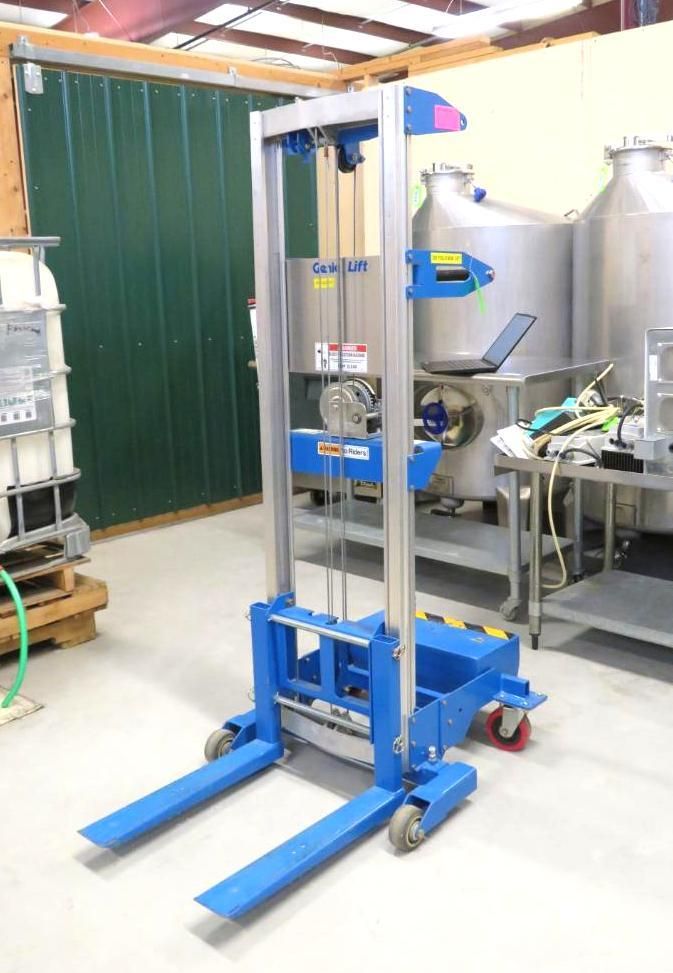 Blue and silver lift cart with forks, in a warehouse setting.