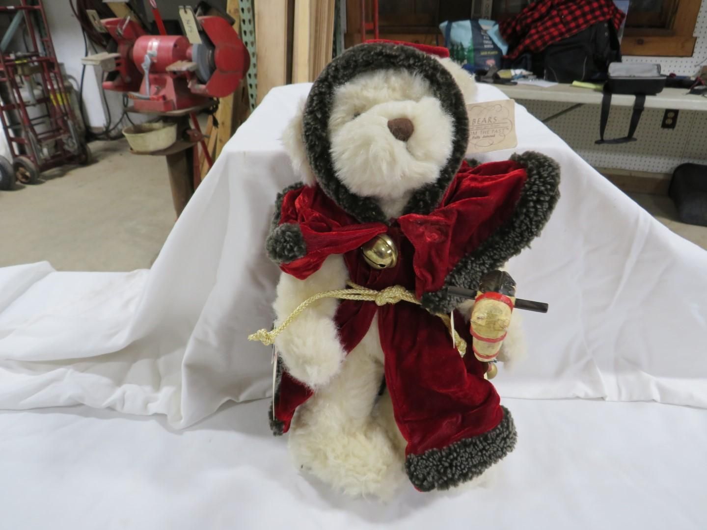 Stuffed bear in red velvet hooded cloak, white fur, bell, sitting on white cloth.