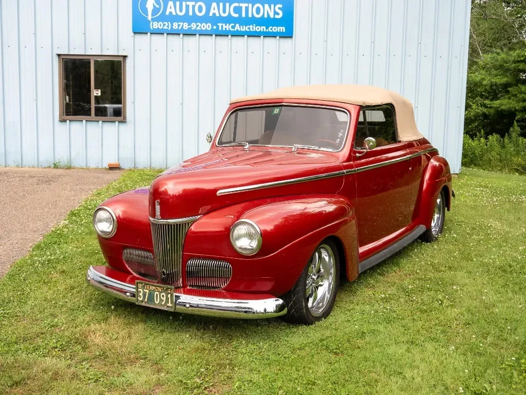 Red convertible classic car in front of a blue auto auction building.