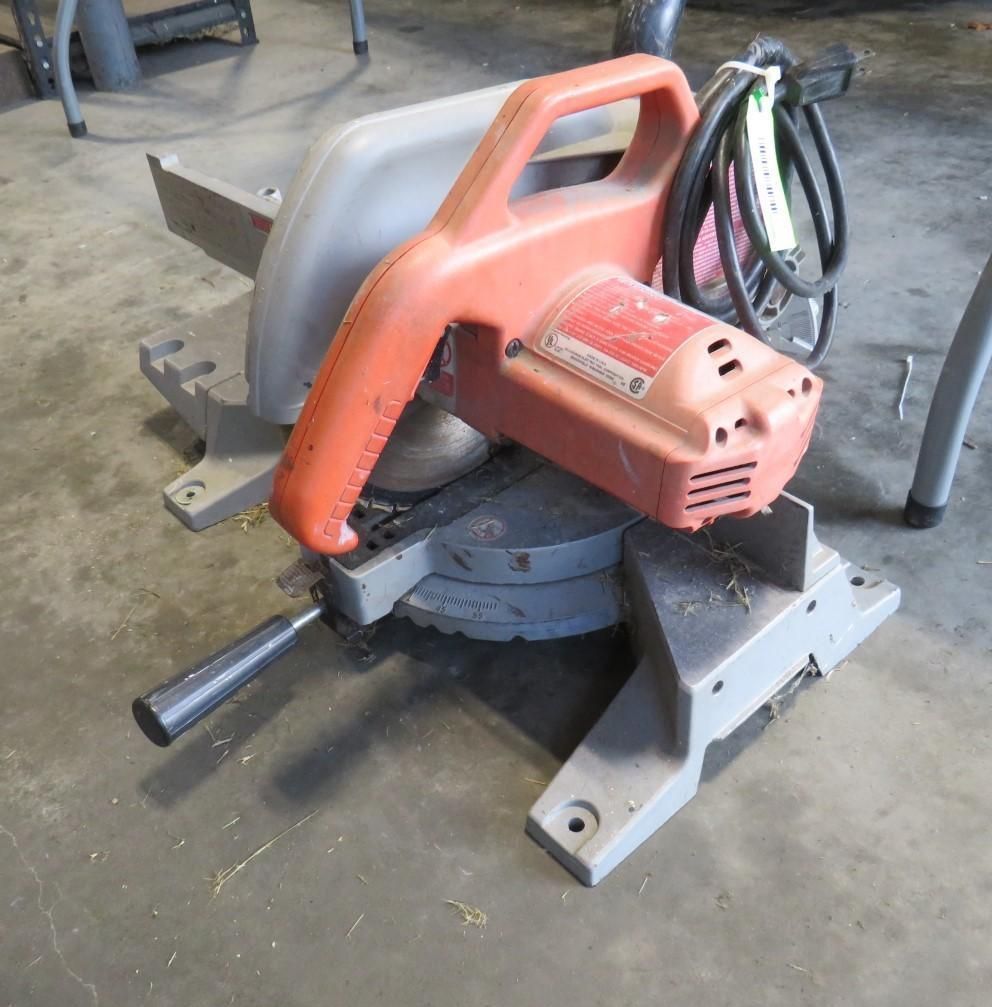 Red and gray miter saw with a black handle and power cord on a concrete surface.
