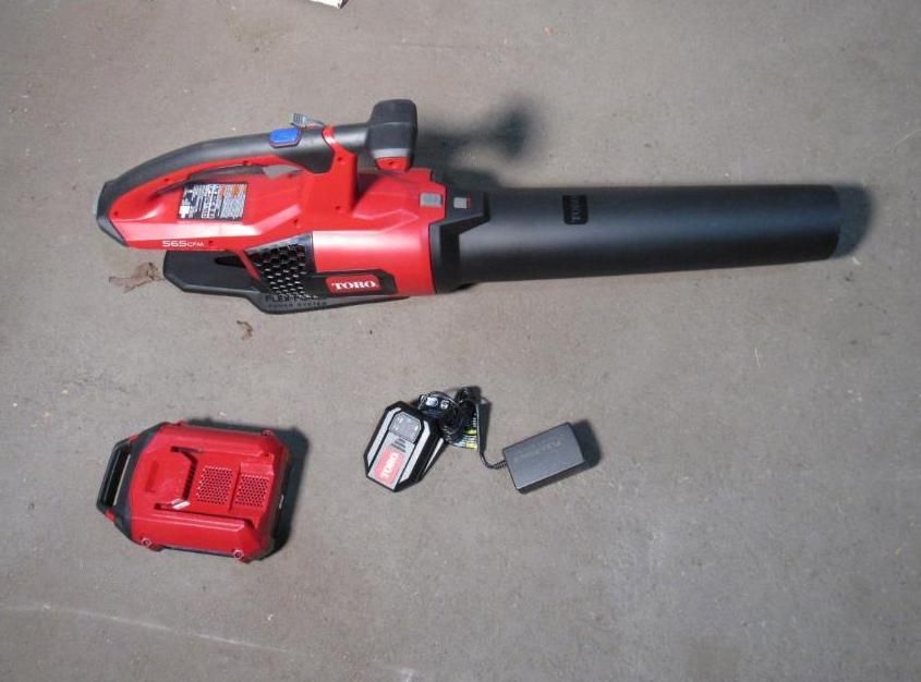 Red and black cordless leaf blower with battery and charger on a gray surface.