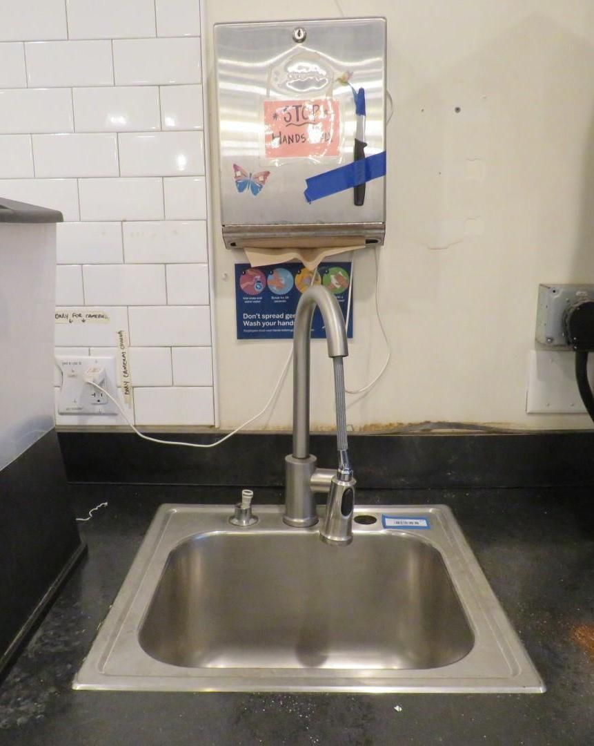 Stainless steel sink with faucet, soap dispenser, paper towel dispenser on wall.