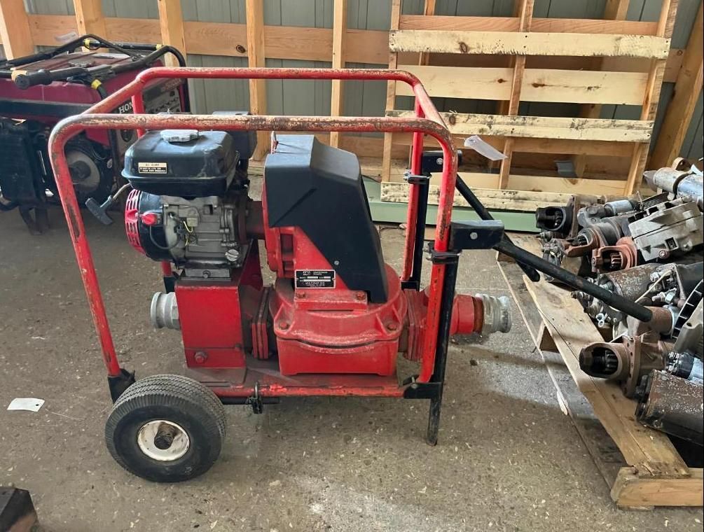 Red water pump with black engine, wheels, and a protective cage, in a storage area.