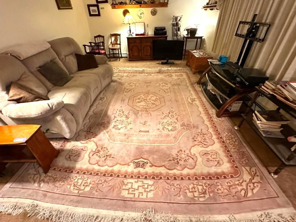 Living room with large pink rug, light-colored sofa, TV, and wooden furniture.