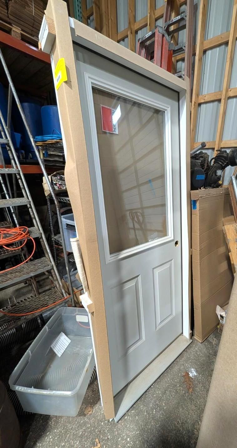 White exterior door with a window, leaning in a workshop or storage area.