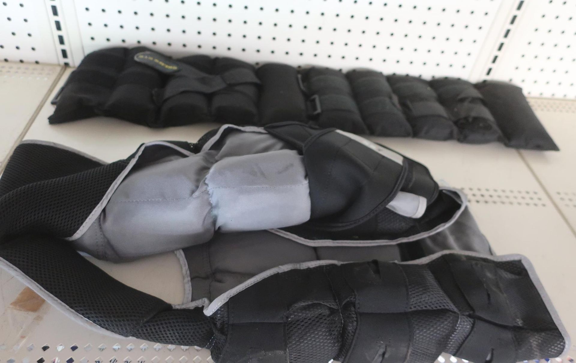 Black and gray weighted exercise vest and separate weighted ankle bands on a shelf.