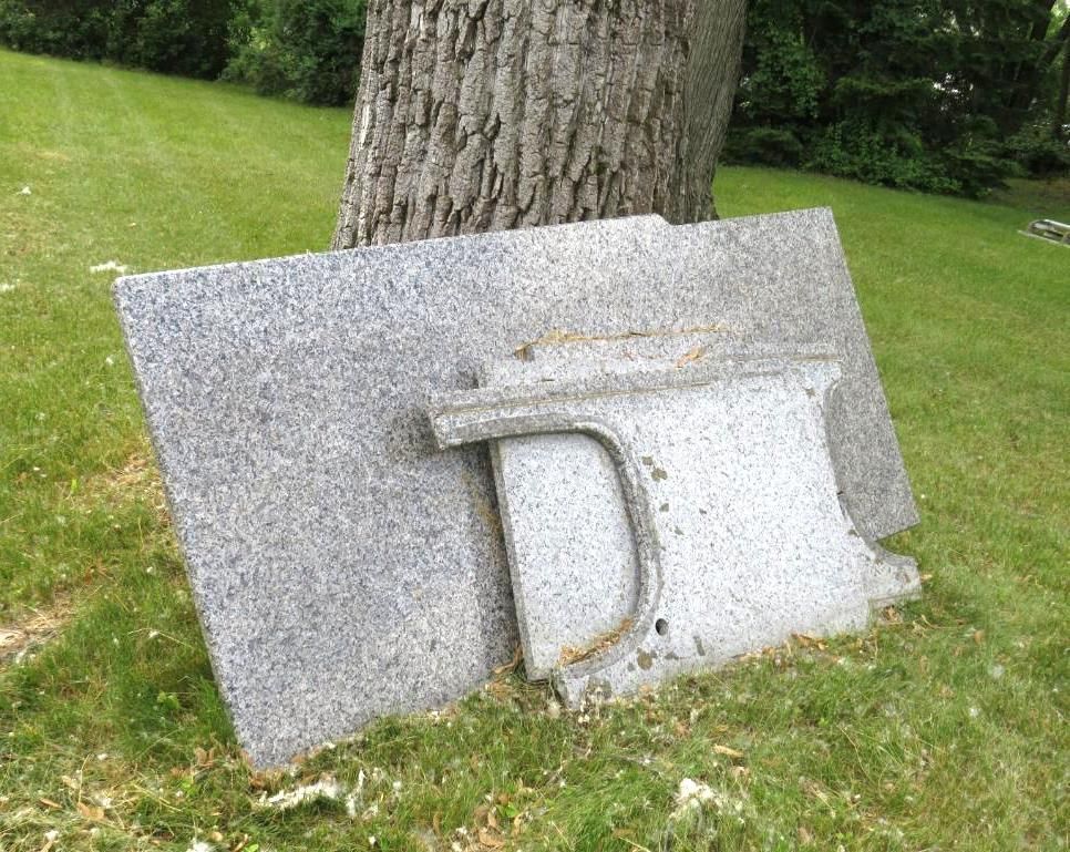 Three granite headstone pieces laying on green grass near a tree.