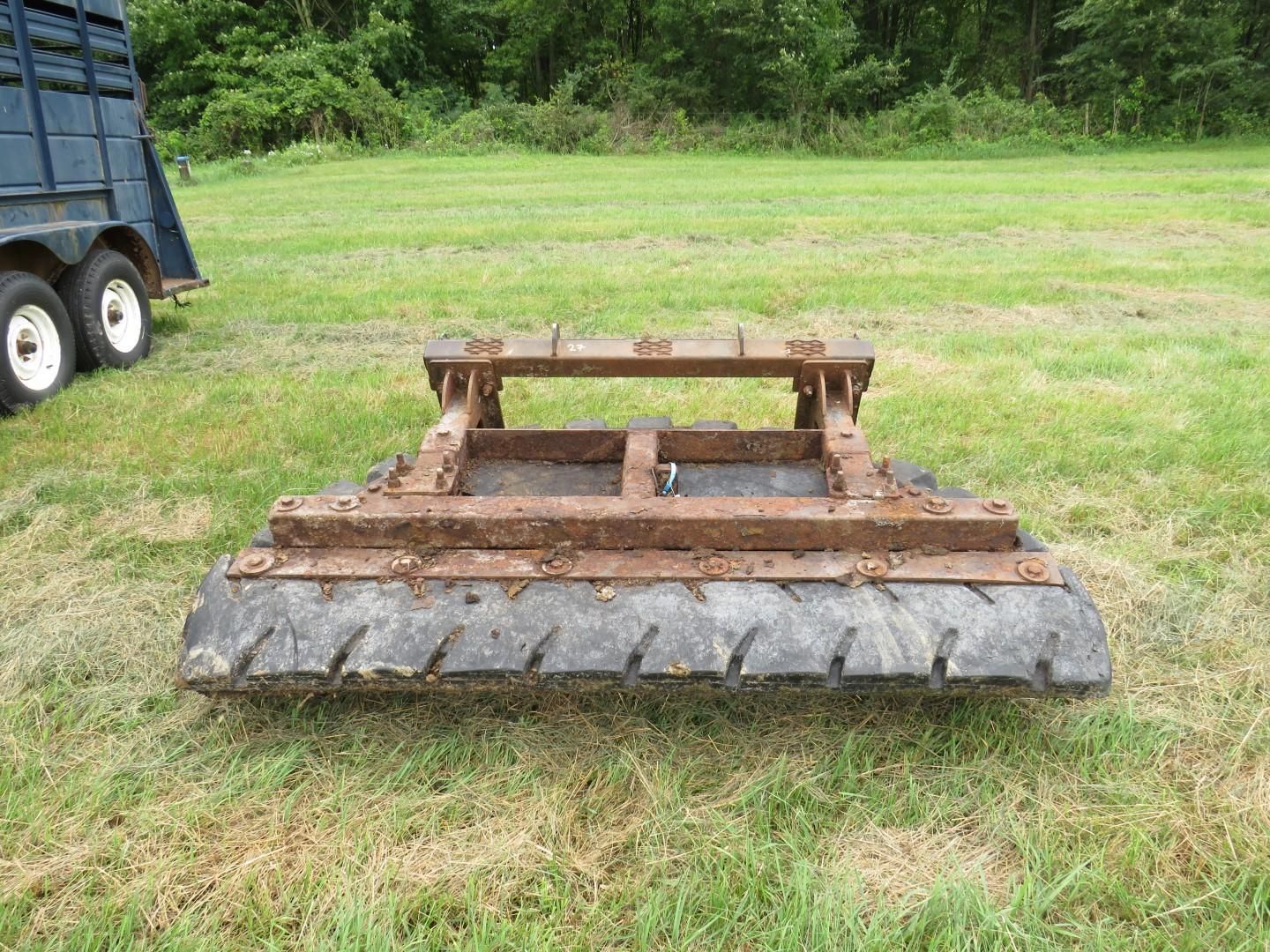 A heavy tire drag with metal framework rests on grass, with a trailer in the background.