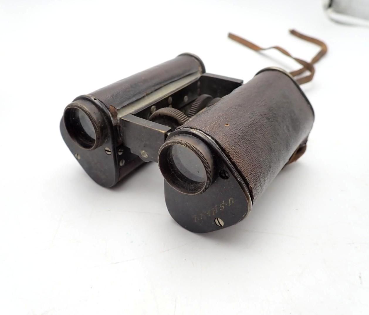 Vintage black binoculars with brown strap on a white background